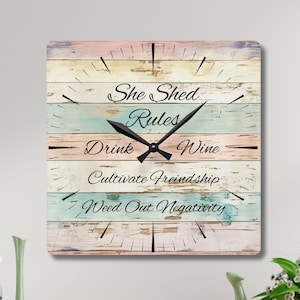 May include: A square clock with a distressed woodgrain design. The clock face features the text "She Shed Rules" and a list of rules: "Drink Wine", "Cultivate Friendship", and "Weed Out Negativity".