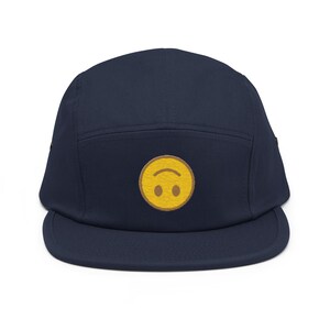 May include: A navy blue 5-panel cap with a yellow upside-down smiley face embroidered on the front.