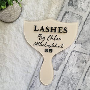 May include: A white acrylic hand mirror with the text "Lashes By Chloe @thelashhut" and Instagram and TikTok icons.