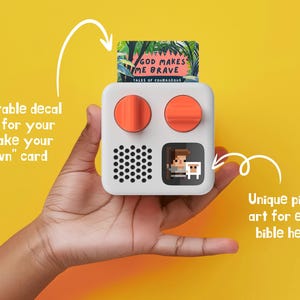 May include: A white, square-shaped device with two orange buttons and a pixelated image of a person and a sheep. The device has a black speaker grille and a slot for a card that says "God Makes Me Brave, Tales of Courageous".