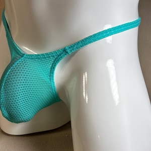 May include: A turquoise thong made of a mesh fabric. The garment has a pouch in the front and thin straps. The thong is displayed on a white mannequin.