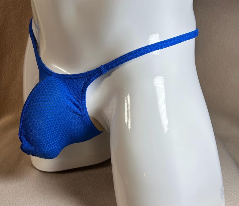 May include: A blue thong-style swimsuit bottom with a textured, breathable pouch. The garment features a thin waistband and side straps. The swimsuit is displayed on a white mannequin.