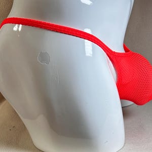 May include: Bright red mesh underwear with a thong-style back. The pouch is designed with a breathable mesh fabric. The underwear is displayed on a white mannequin.
