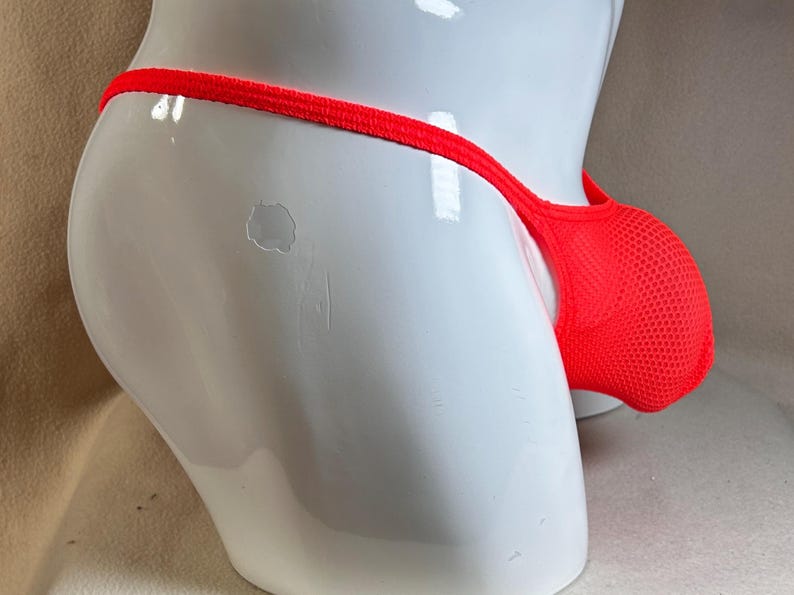 May include: Bright red mesh underwear with a thong-style back. The pouch is designed with a breathable mesh fabric. The underwear is displayed on a white mannequin.