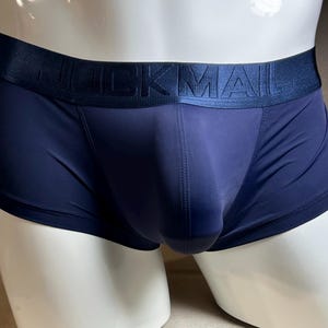 Puede incluir: Bóxers azul marino con la palabra "MUCKMAIL" impresa en la cintura. La ropa interior se muestra en un maniquí blanco. La tela parece suave y ajustada.