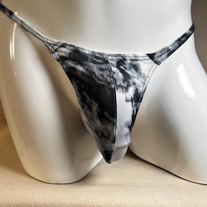 Könnte beinhalten: Ein String-Unterwäsche mit einem schwarz-weißen abstrakten Muster. Der Stoff scheint ein weiches, leichtes Material zu sein. Das Kleidungsstück wird auf einer weißen Schaufensterpuppe präsentiert.