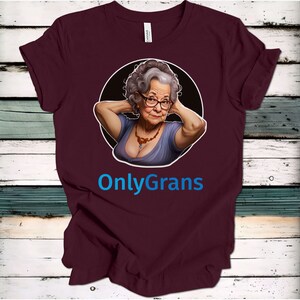 May include: A maroon t-shirt with a circular graphic of an older woman with gray hair wearing a purple top and a necklace. The text "OnlyGrans" is printed in blue below the graphic.