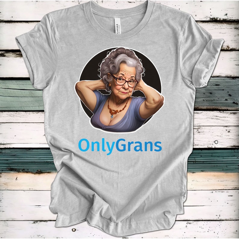 May include: A gray t-shirt with a cartoon image of an older woman with gray hair and glasses. The woman is wearing a blue dress and a necklace. The text "OnlyGrans" is printed in blue below the image.
