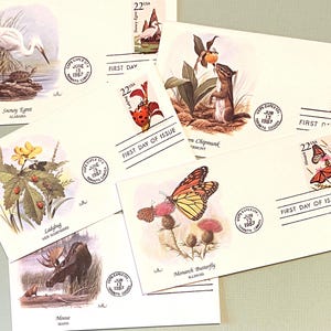 May include: A collection of six First Day of Issue envelopes featuring different animals and insects from various states. The envelopes are cream-colored with a red, white, and blue stamp in the upper right corner. The envelopes feature illustrations of a snowy egret, a ladybug, a moose, a chipmunk, a monarch butterfly, and a butterfly.