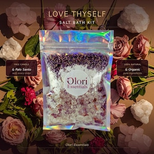 May include: A holographic bag labeled "Salt Bath Kit" with the text "Love Thyself." The bag contains bath salts, lavender, and rose petals. The brand name "Olori Essentials" is visible. The image is surrounded by roses and crystals.