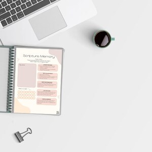 May include: A white and pink planner with the title "Scripture Memory" and a section for writing down a scripture verse. The planner has a spiral binding and a section for tracking progress.