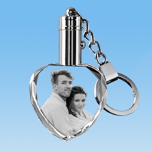 May include: A silver heart-shaped crystal keychain with a photo of a couple inside. The keychain has a silver ring and a silver cap on top.