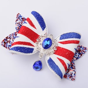 May include: A white, red, and blue bow with a Union Jack design. The bow has a silver and blue jeweled embellishment in the center and a dangling blue jewel.