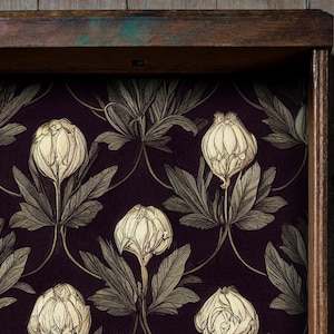 Op de afbeelding: Een houten displaybox met een donkerpaars bloemenpatroon. Het patroon heeft crèmekleurige bloemknoppen en bladeren. Het frame is donkerbruin met een vleugje groen op de bovenrand.