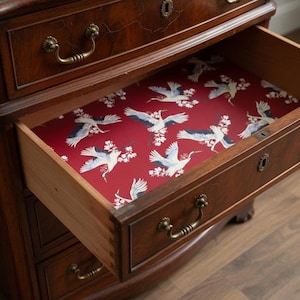 Fabric peel and stick drawer liner in a bold red background with elegant flying cranes and white cherry blossoms. This vintage-inspired contact paper adds a dramatic and artistic flair to any drawer, shelf, or cabinet. Ideal for kitchens, bathrooms, and antique furniture, the self-adhesive liner is easy to apply and remove. A perfect floral contact paper for those who love retro, Asian-inspired, or maximalist home décor. Stylish and functional for renters and homeowners alike.