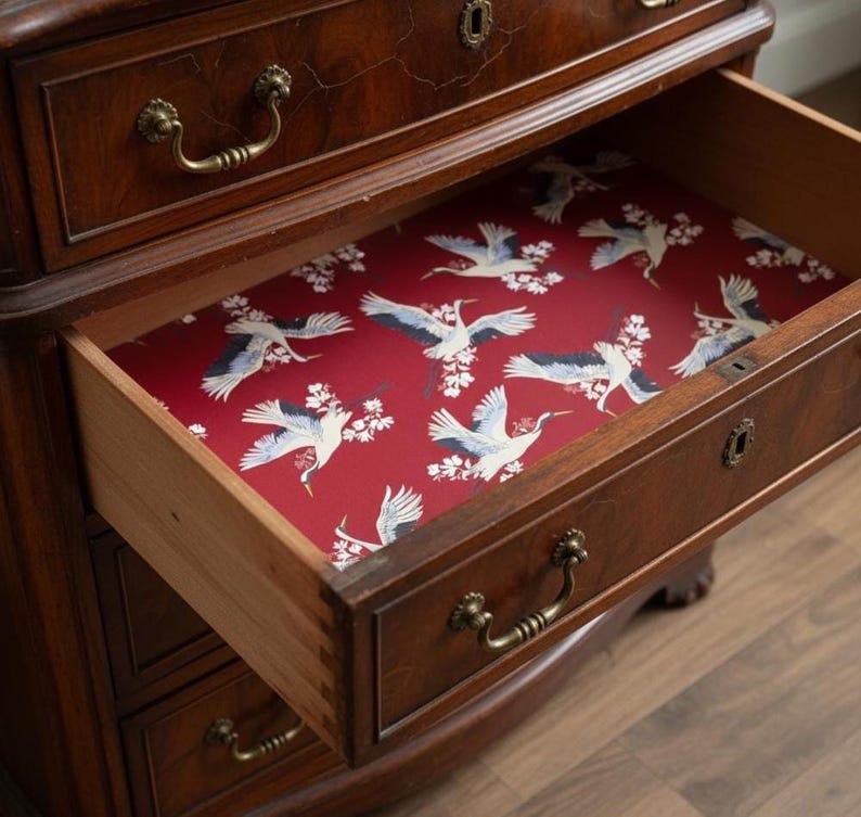 Fabric peel and stick drawer liner in a bold red background with elegant flying cranes and white cherry blossoms. This vintage-inspired contact paper adds a dramatic and artistic flair to any drawer, shelf, or cabinet. Ideal for kitchens, bathrooms, and antique furniture, the self-adhesive liner is easy to apply and remove. A perfect floral contact paper for those who love retro, Asian-inspired, or maximalist home décor. Stylish and functional for renters and homeowners alike.