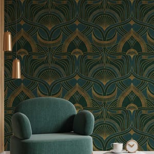 Op de afbeelding: Een groene fluwelen fauteuil met gouden metalen poten staat voor een muur met een donkergroen en gouden geometrisch patroon behang. Een witte bijzettafel met een kopje en een klok staat naast de fauteuil.
