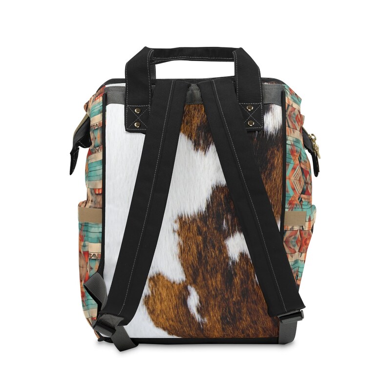Pu&ograve; includere: Uno zaino marrone e bianco con motivo in pelle di mucca, con spalline nere e un motivo geometrico turchese, arancione e marrone sui lati.