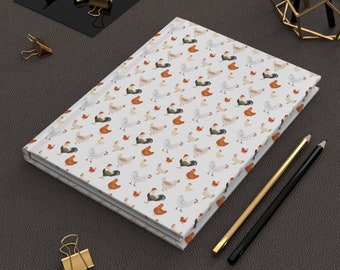 May include: A white notebook with a repeating pattern of colorful chickens. The notebook is closed and lying on a dark brown surface.