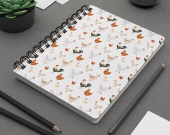 May include: A white spiral bound notebook with a repeating pattern of colorful chickens. The notebook is on a gray surface with a pencil and a glass of water.