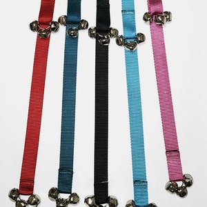May include: Five dog training bell collars in different colors: red, blue, black, turquoise, and pink. Each collar has three silver bells attached.