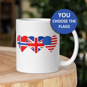 May include: White ceramic mug featuring three heart-shaped flags: Norway, United Kingdom, and the United States. The mug has a white handle and the text "YOU CHOOSE THE FLAGS" on a blue circle.