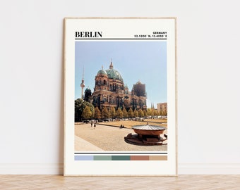 May include: A framed print of the Berlin Cathedral in Germany. The print features a photo of the cathedral with a blue sky and green trees in the foreground. The print also includes the coordinates of Berlin: 52.5200° N, 13.4050° E. The print has a color palette of light blue, green, brown, and beige.