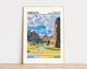 May include: A framed print of a landscape scene with a river winding through a valley with rocky cliffs. The print has a color palette of blue, green, and yellow. The text "OREGON" and "UNITED STATES 43.8041° N, 120.5542° W" is printed at the top of the print.