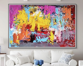 Puede incluir: Pintura abstracta con pinceladas audaces de pintura amarilla, rosa, azul, roja y naranja. La pintura está enmarcada en un marco fino plateado y cuelga sobre un sofá blanco en una sala de estar.