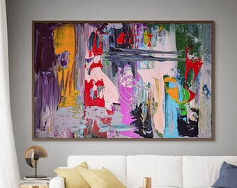 Puede incluir: Pintura abstracta con trazos audaces de rojo, amarillo, azul, verde, rosa y morado sobre un lienzo blanco. La pintura está enmarcada en un marco de madera oscura y cuelga de una pared gris sobre un sofá blanco.