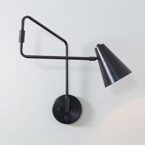 Può includere: Applique da parete nera con braccio geometrico e paralume a forma di cono nero.