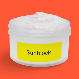 May include: A white jar of sunscreen with a yellow label that reads "Sunblock" in black text. The sunscreen has a thick, creamy texture. The jar is set against an orange background.