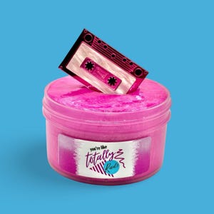 May include: A pink container of slime with a retro cassette tape on top. The container has a label with the text "you're like totally Rad!" on it. The background is a solid blue.