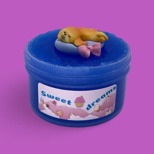 May include: A blue container of slime with a sleeping dog figurine on top. The container has a label with the words "Sweet dreams" and illustrations of sweets.