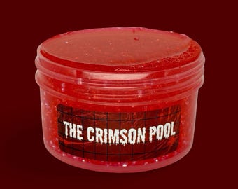 May include: A clear, round plastic container filled with a vibrant red, glittery, gel-like substance. A rectangular label on the front features a black grid pattern and the white text THE CRIMSON POOL in a stylized, dripping font.