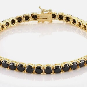 Puede incluir: Un brazalete de cadena de tenis de oro con piedras redondas negras. El brazalete está hecho de oro y tiene un cierre de broche.