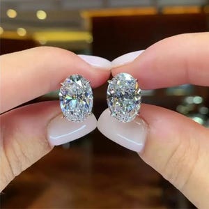 May include: A pair of oval-shaped diamond earrings set in silver. The earrings are large and sparkly.