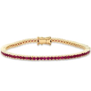 Könnte beinhalten: Ein goldenes Tennisarmband mit einer Reihe roter Rubin-Steine.