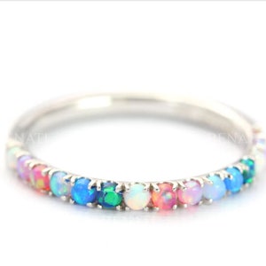 Könnte beinhalten: Ein Silberring mit einer Reihe von Opal-Edelsteinen in Regenbogenfarben, die in einer Krappenfassung sitzen.