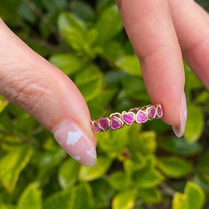Könnte beinhalten: Ein Goldring mit einer Reihe von rosafarbenen herzförmigen Edelsteinen.