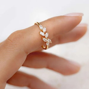 Könnte beinhalten: Ein goldener Ring mit einem zarten Design aus Blättern und kleinen, klaren Steinen.