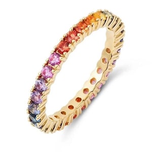 Könnte beinhalten: Ein goldfarbener Ring mit einem durchgehenden Band aus bunten Edelsteinen. Die Edelsteine wechseln von Orange zu Rot, Rosa, Lila und Blau. Der Ring ist eine durchgehende Schleife aus Edelsteinen, die in einem goldenen Band gefasst sind.