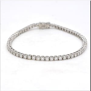 Könnte beinhalten: Ein silbernes Tennisarmband mit einer Reihe kleiner, runder Diamanten.