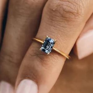 Könnte beinhalten: Ein zarter Goldring mit einem blauen Edelstein im Smaragdschliff.