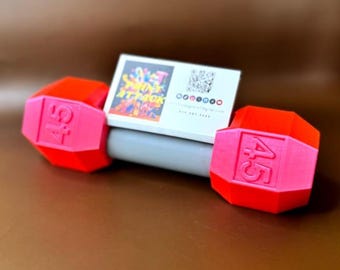 May include: A red and pink dumbbell with a business card on top. The business card has a colorful design and the text "Spring Attack" on it.