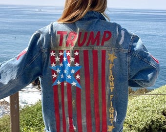 May include: A blue denim jacket with a painted American flag design on the back. The flag is red, white, and blue with gold stars. The words "TRUMP" and "FIGHT FIGHT" are painted on the jacket in red and gold.