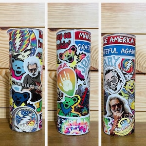May include: A white tumbler with a colorful design featuring a variety of stickers. The stickers include images of Jerry Garcia, the Grateful Dead logo, and the words "Keep on Truckin'" and "Make America Grateful Again".
