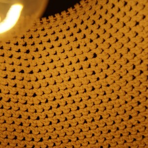 Op de afbeelding: Close-up van een geweven stof met een textuur, ruitvormig patroon in een warme, mosterdgele kleur.