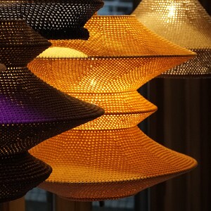 Op de afbeelding: Een set van drie geweven hanglampen met een gelaagd, trapsgewijs ontwerp. De lampen zijn gemaakt van een natuurlijk materiaal en hebben een warme, uitnodigende gloed.