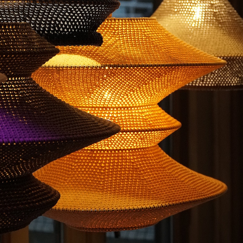 Op de afbeelding: Een set van drie geweven hanglampen met een gelaagd, trapsgewijs ontwerp. De lampen zijn gemaakt van een natuurlijk materiaal en hebben een warme, uitnodigende gloed.